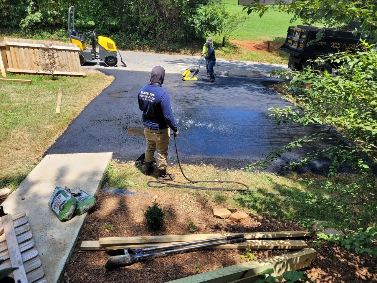 Sealcoat going down on a driveway, the wet black coat beside the old surface